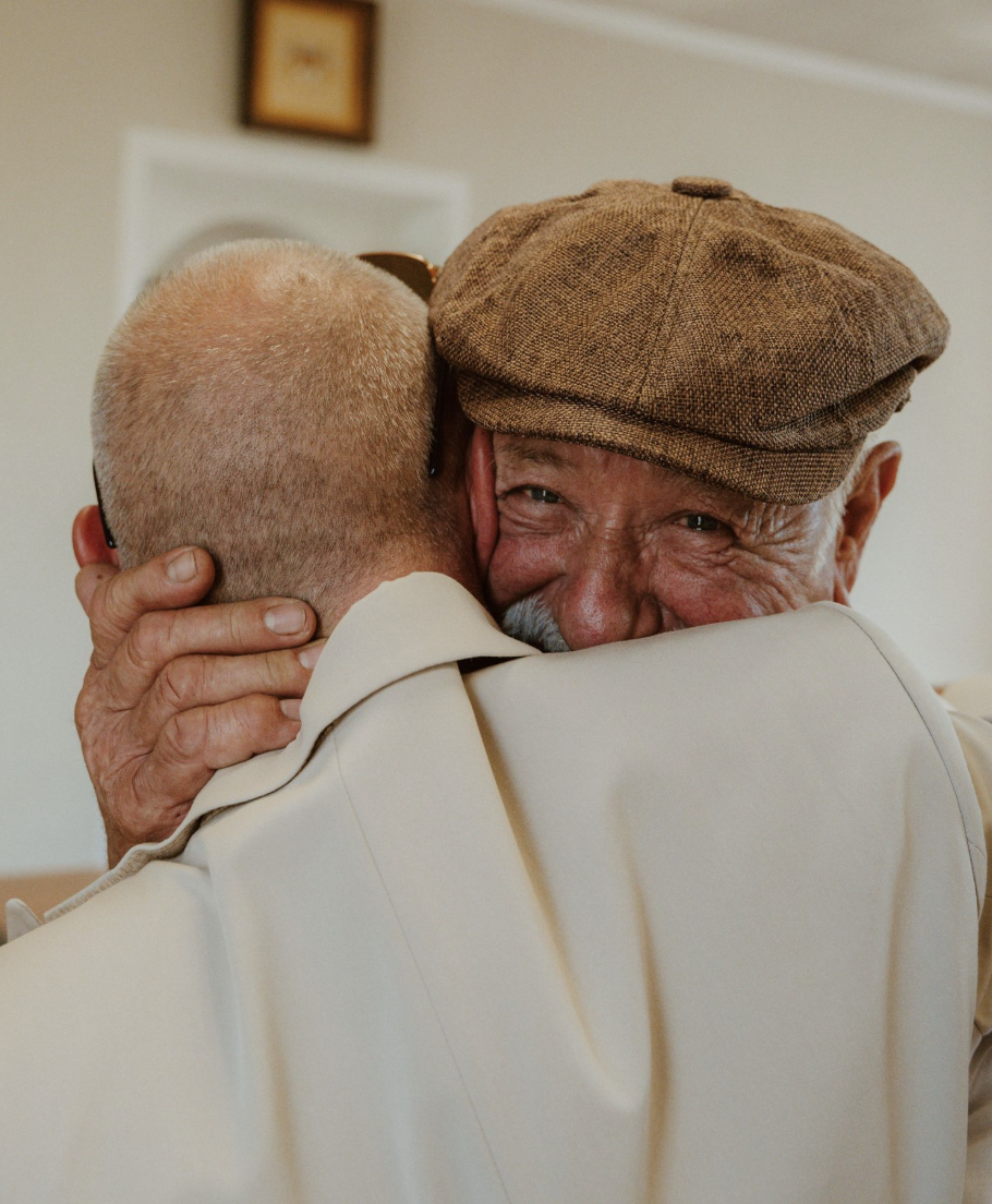 Deux hommes s’étreignent pendant un mariage, un regard ému par-dessus l’épaule
